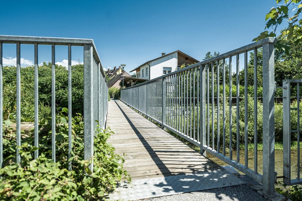 Brücke für Fußgänger mit einem feuerverzinkten Edelstahl-Geländer mit Pflanzen am Flussufer