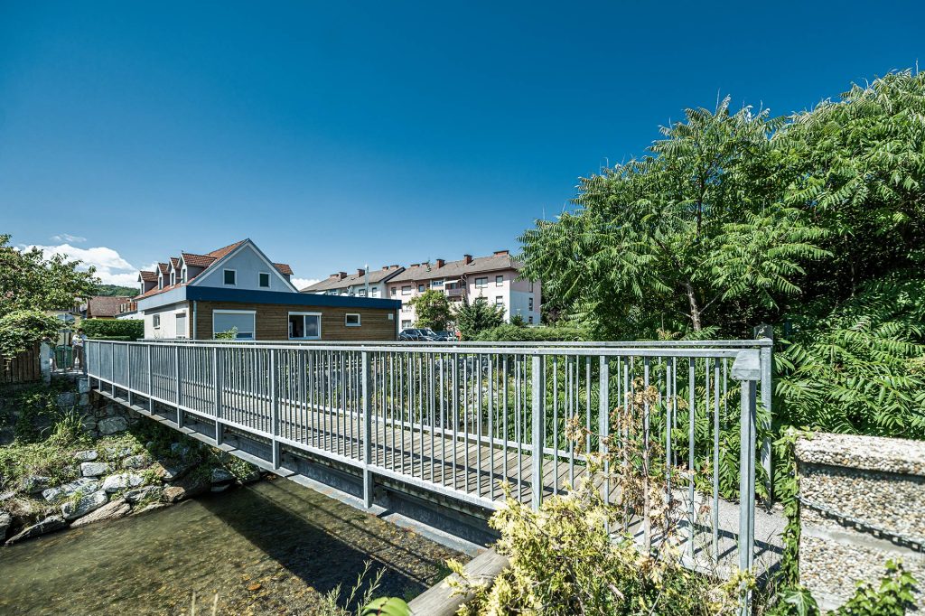 Brücke für Fußgänger mit einem feuerverzinkten Edelstahl-Geländer mit Pflanzen am Flussufer